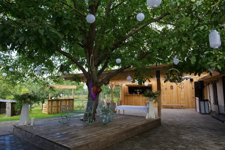 Außenbereich im Bruders Schopf Oberkirch: Holzterrasse mit Baum, Laternen, rustikaler Bar und romantischer Hochzeitsdekoration.