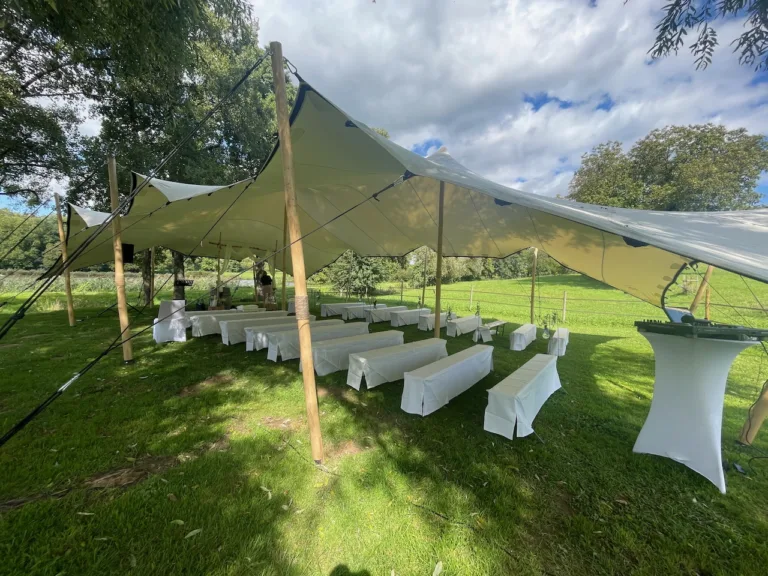 Freie Trauung im Haus am Teich: Outdoor-Zeremonie unter Stretchzelt mit weißen Bänken und grünem Wiesenambiente.
