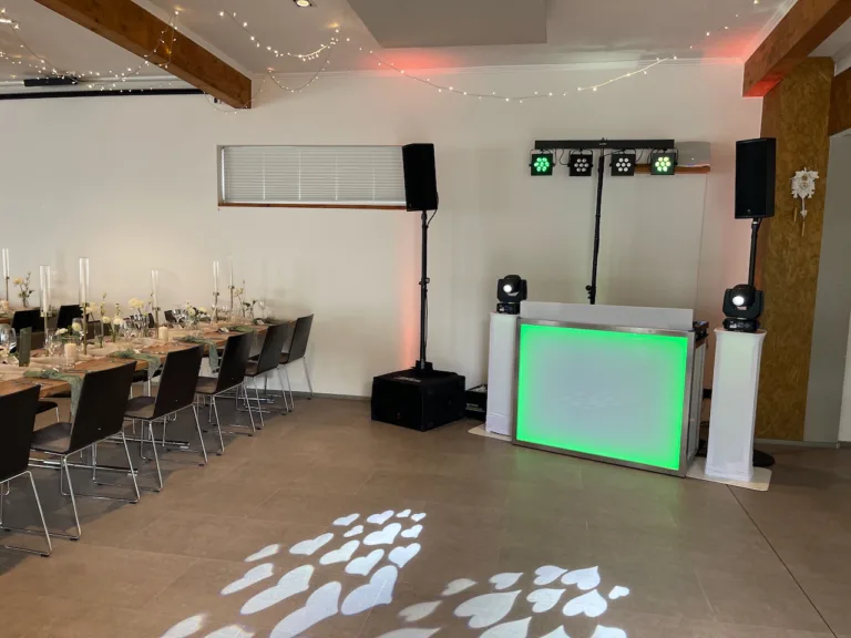 DJ-Pult mit Lichttechnik im Hochzeitssaal des Weinguts Bieselin in Ettenheim, festlich gedeckte Tafeln und stimmungsvolle Herzprojektionen.