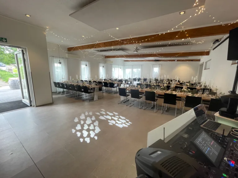 Hochzeitssaal im Weingut Bieselin in Ettenheim, festlich dekoriert mit Tafeln, Kerzen und Lichterketten, Blick vom DJ-Pult mit Lichttechnik.